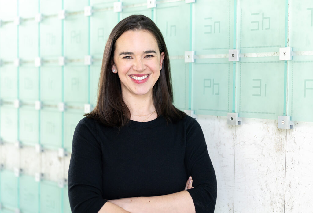 Danielle Doughty smiles in front of a glass sculpture of the periodic table of elements.