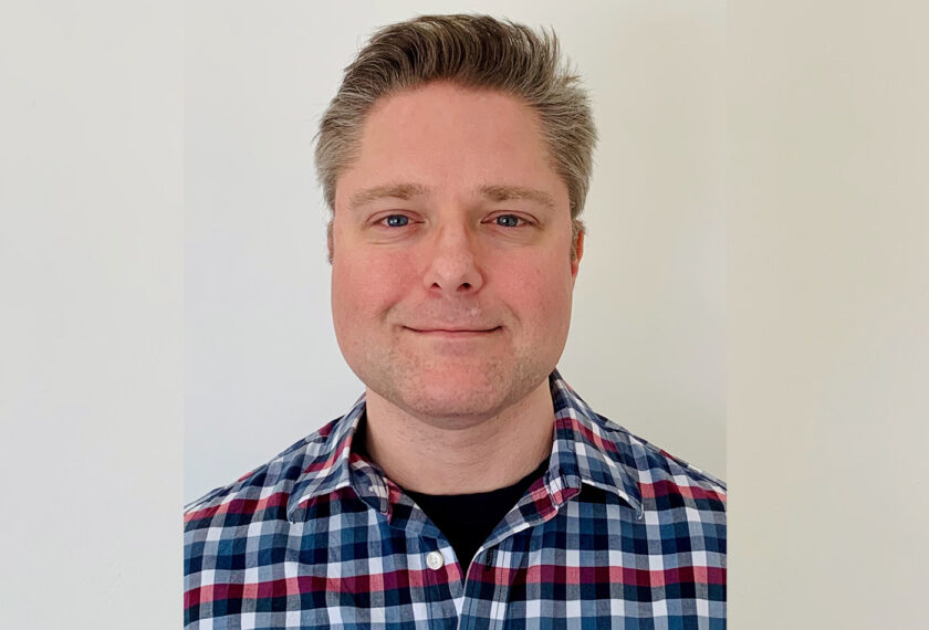 Chris Kriofske smiles in front of a beige wall.