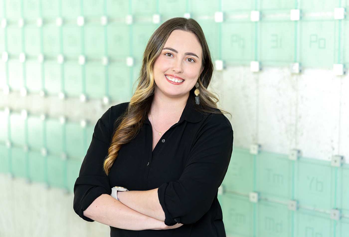 Lexy Wynne smiles in front of a glass sculpture of the periodic table of elements.