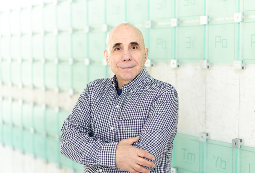 Brian Pretti smiles in front of a glass sculpture of the periodic table of elements.