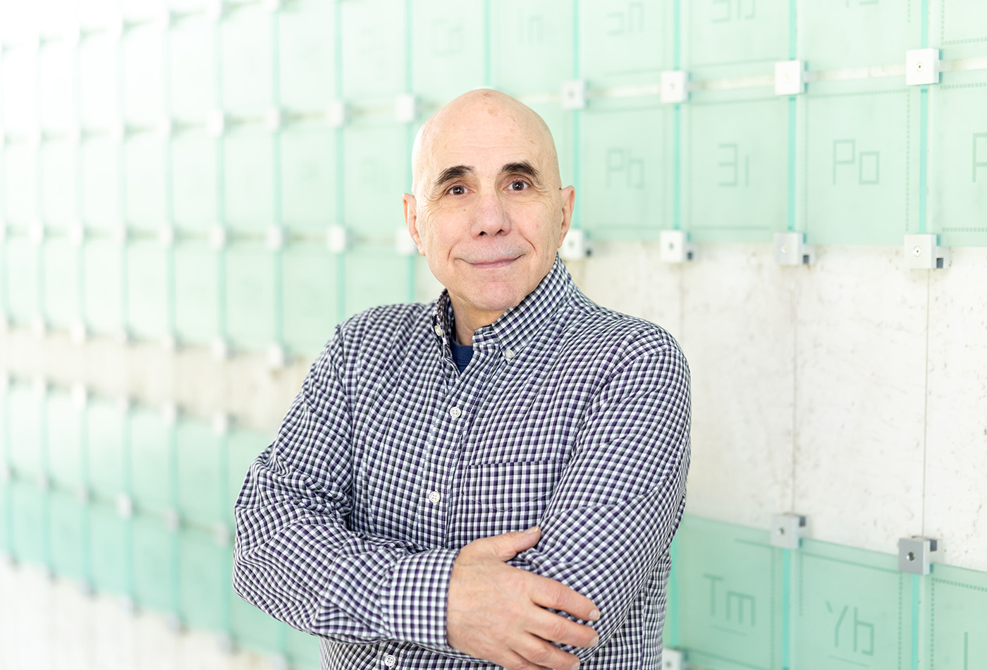 Brian Pretti smiles in front of a glass sculpture of the periodic table of elements.