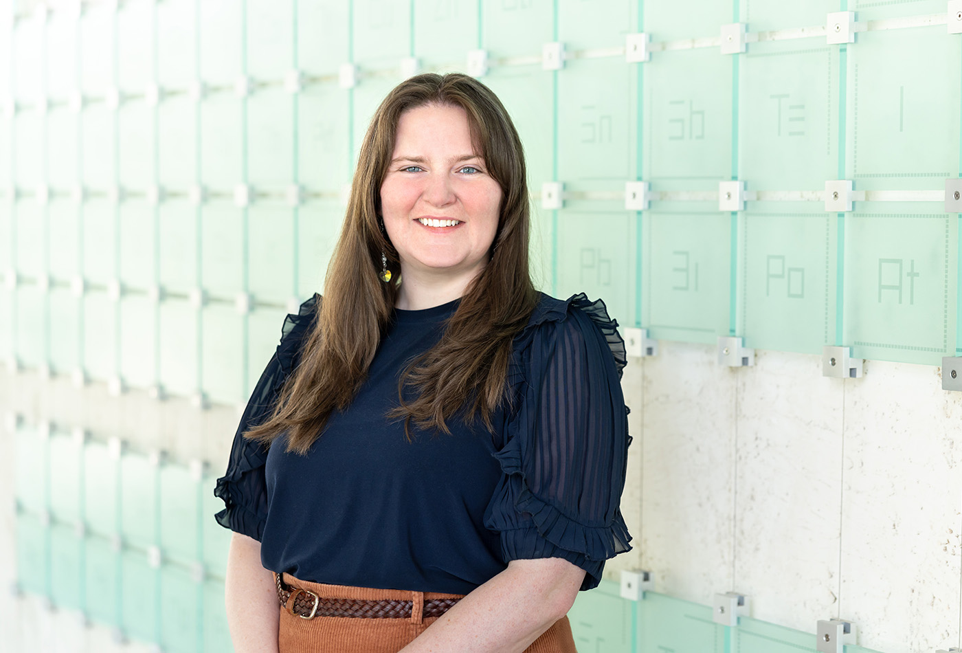 Rebecca Reid smiles in front of a glass sculpture of the periodic table of elements.