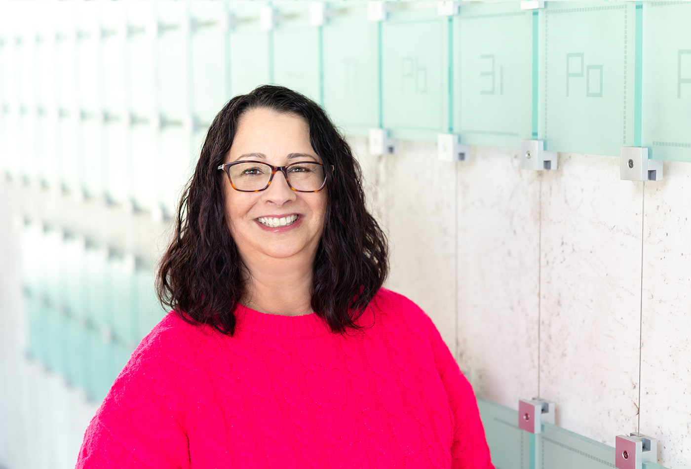 Jennifer Weisman smiles in front of a glass sculpture of the periodic table of elements.