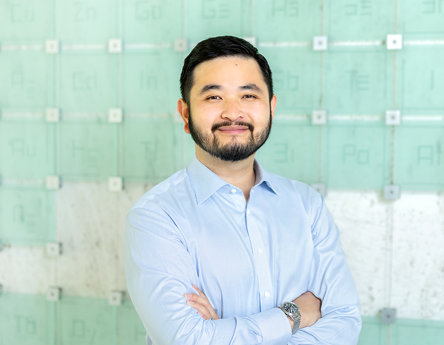 Danny Thach smiles in front of the Periodic Table.