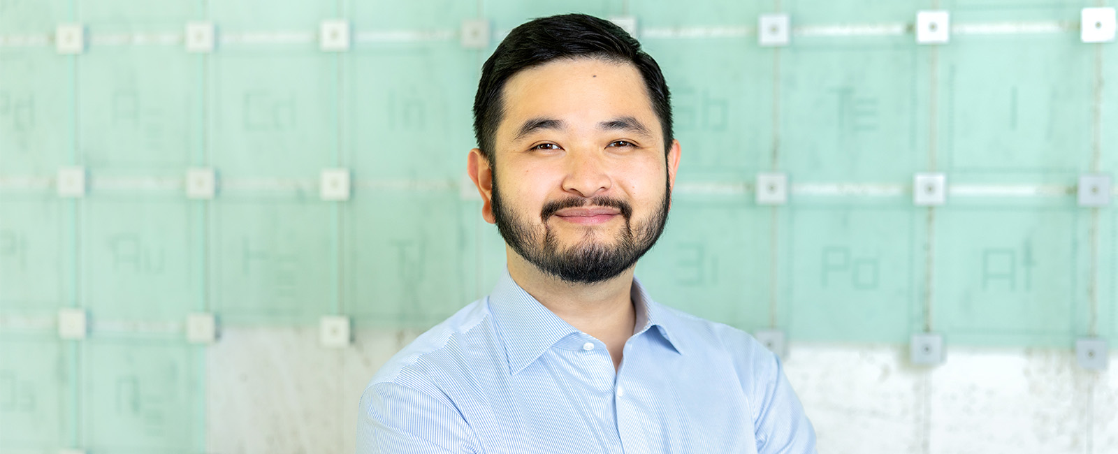 Danny Thach smiles in front of the Periodic Table.