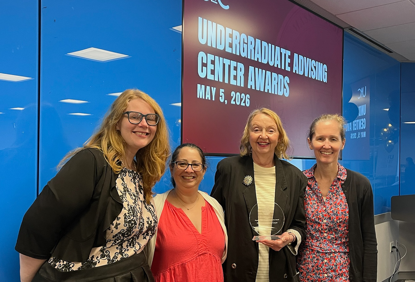 Four women smile in front of a screen that says UNDERGRADUATE ADVISING CENTER AWARDS, MAY 5, 2026.