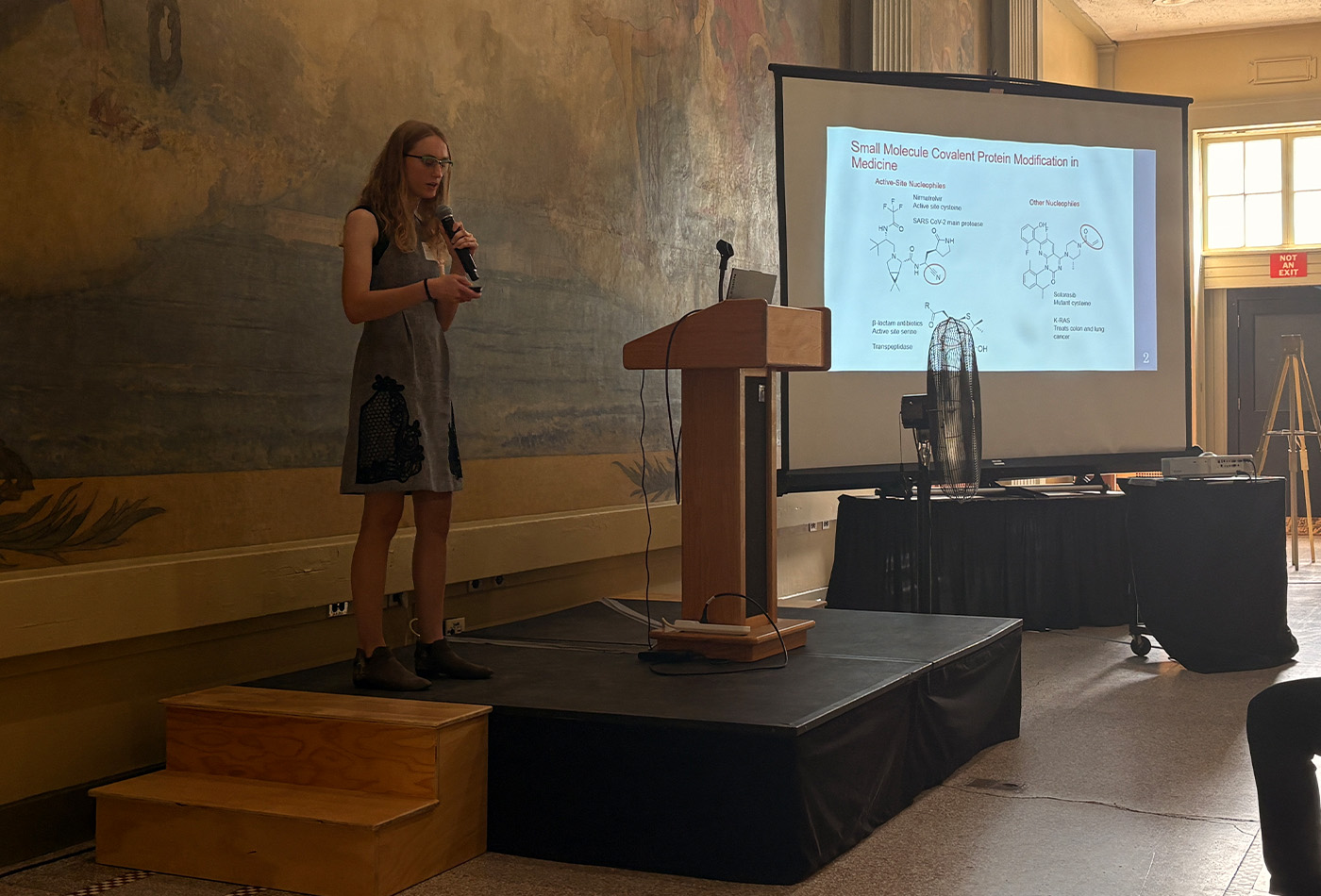 Hallie Trial stands in front of a power point presentation.