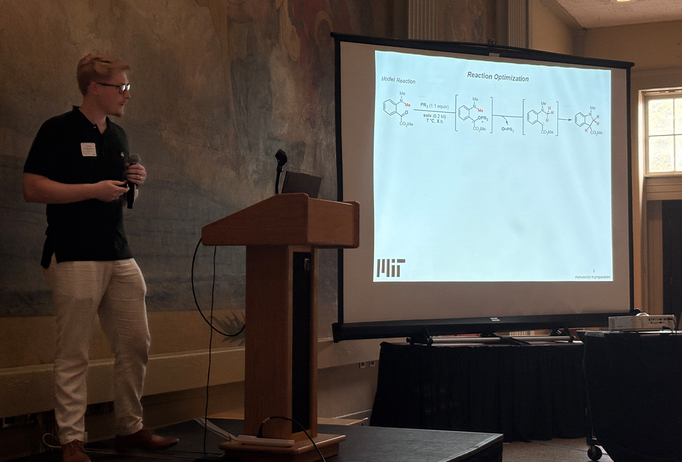 Philip West stands in front of a power point presentation.