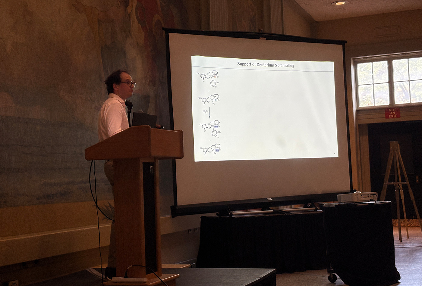 Daniel Rozsar stands in front of a power point presentation.
