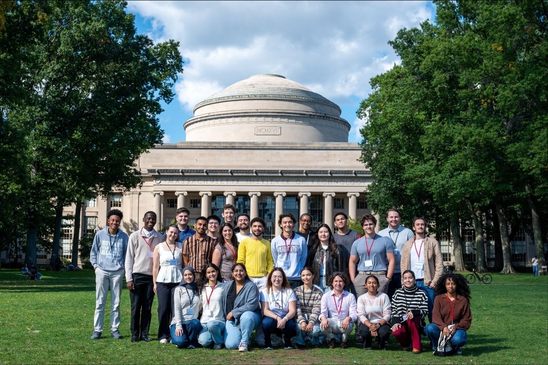 A group of 26 student participants in the MIT ACCESS program pose as a group in front of MIT's Killian Court. A view of the MIT dome is in the background.