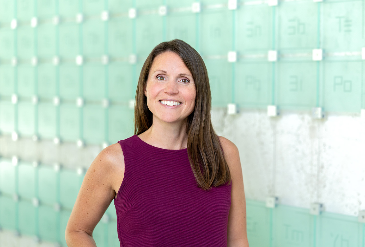 Lexy Wynne smiles in front of a glass sculpture of the periodic table of elements.